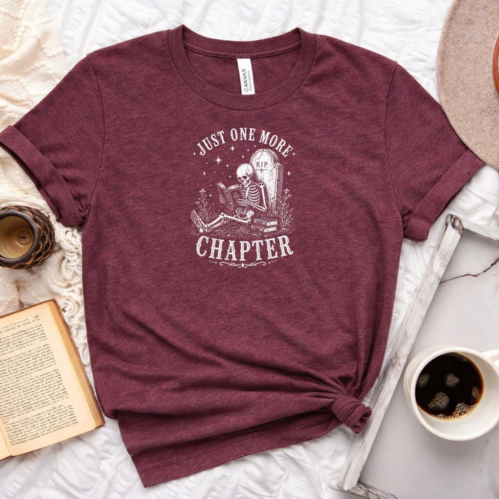 Just One More Chapter unisex tee with vintage skeleton reading in armchair surrounded by stacked books and wildflowers graphic