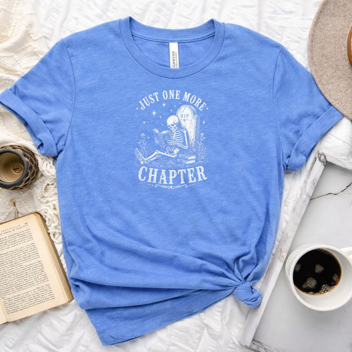 Just One More Chapter unisex tee with vintage skeleton reading in armchair surrounded by stacked books and wildflowers graphic