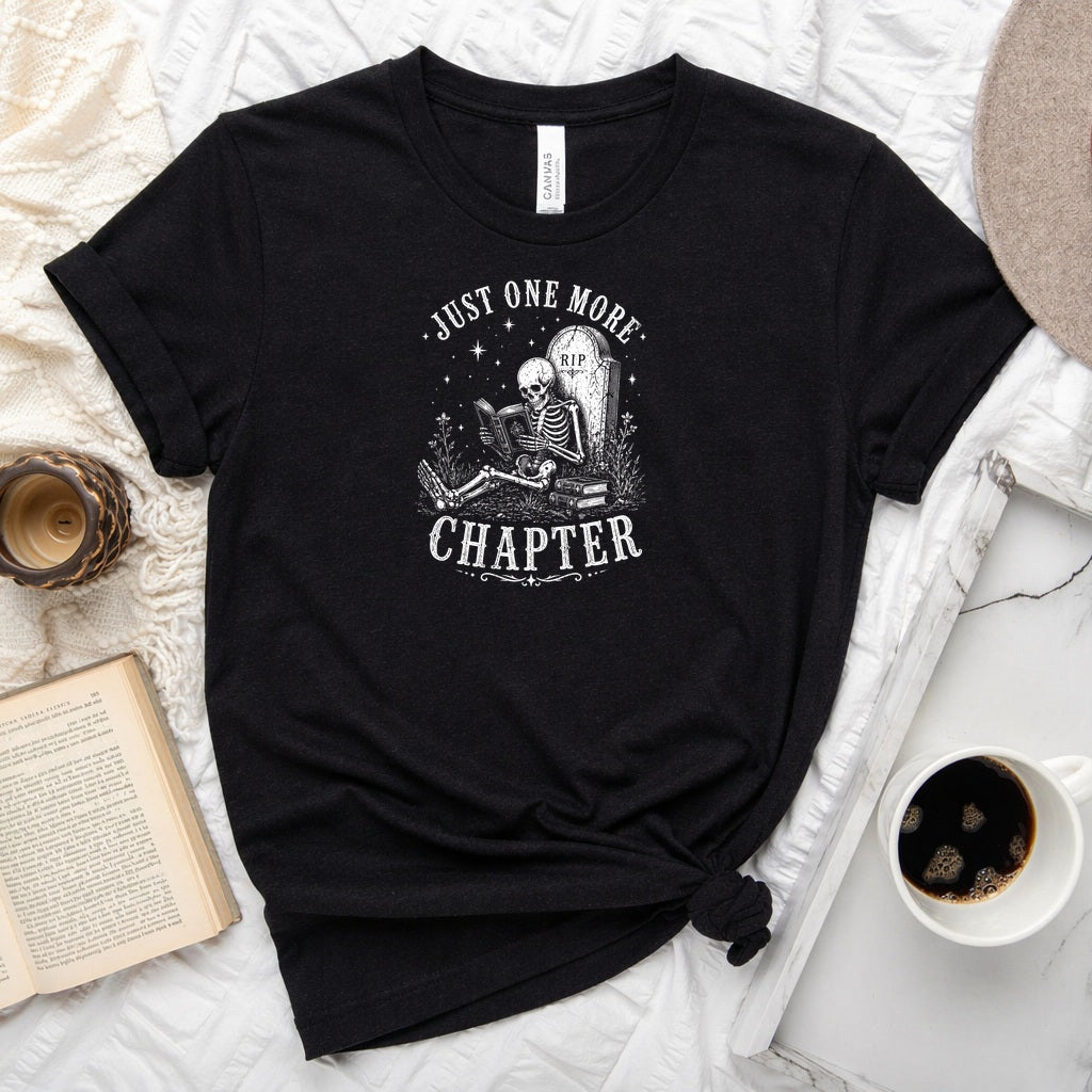 Just One More Chapter unisex tee with vintage skeleton reading in armchair surrounded by stacked books and wildflowers graphic