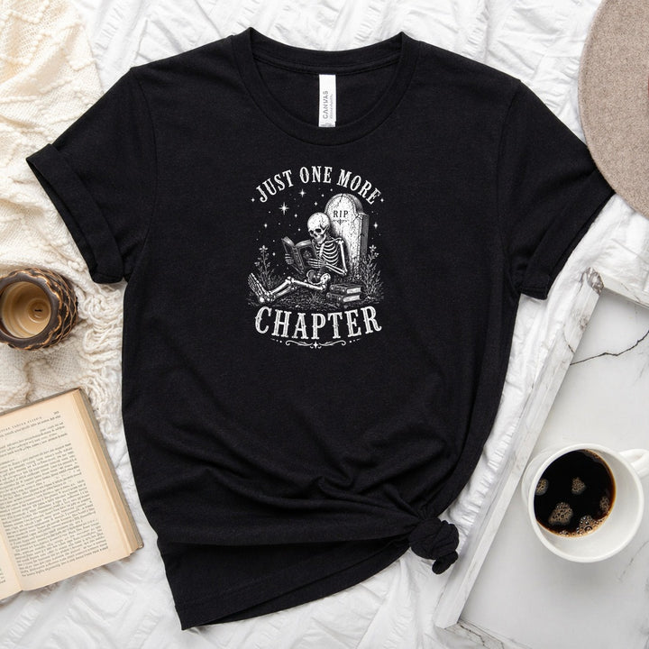 Just One More Chapter unisex tee with vintage skeleton reading in armchair surrounded by stacked books and wildflowers graphic
