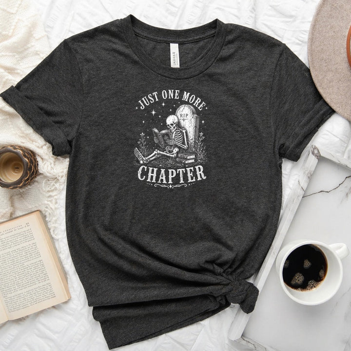 Just One More Chapter unisex tee with vintage skeleton reading in armchair surrounded by stacked books and wildflowers graphic