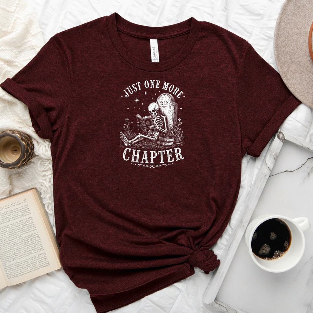 Just One More Chapter unisex tee with vintage skeleton reading in armchair surrounded by stacked books and wildflowers graphic
